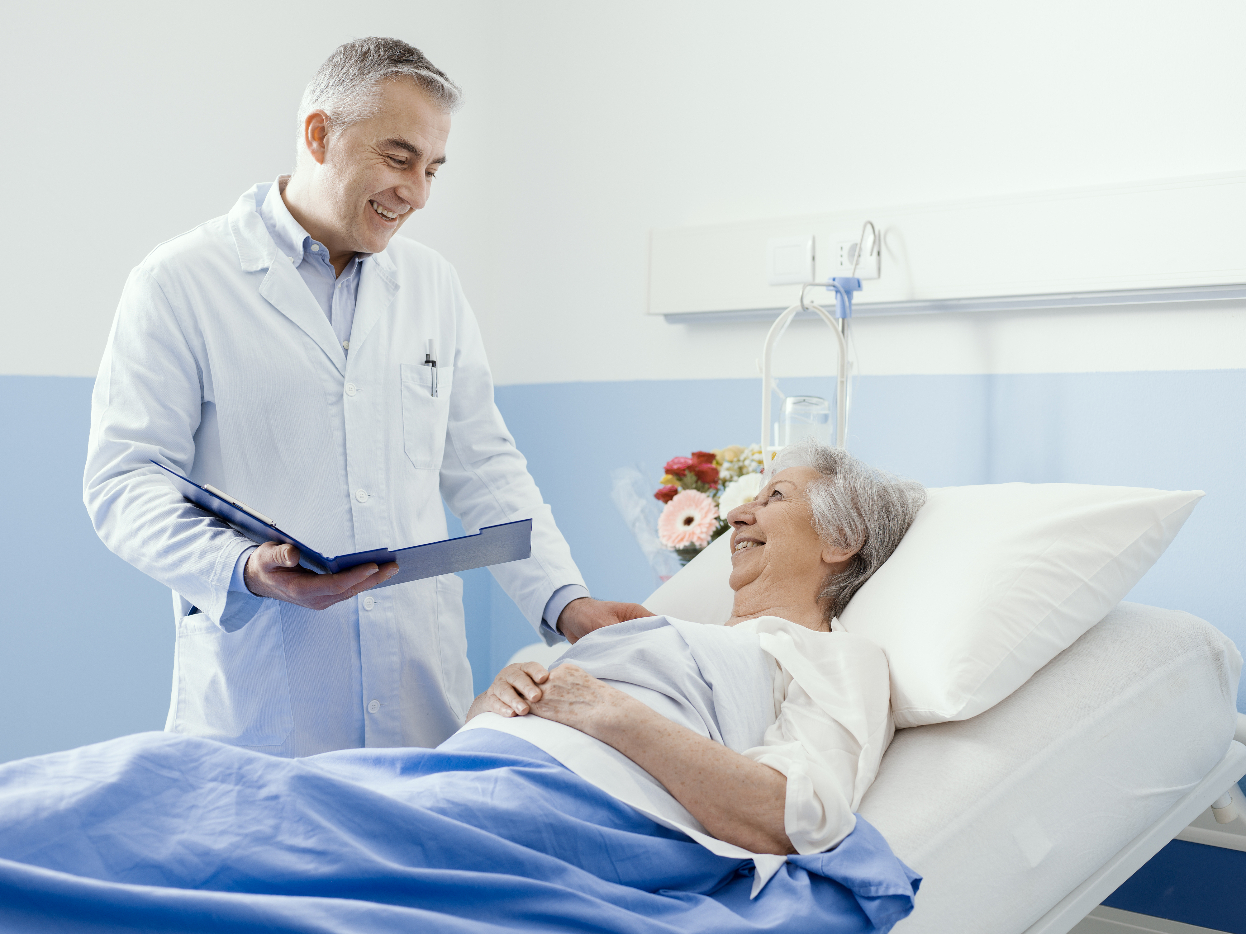 Doctor checking on patient covered with medical blanket in hospital room